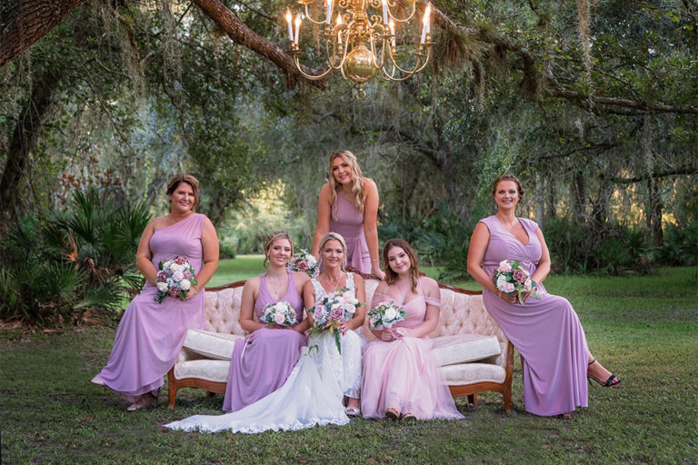 bride and bridesmaids outdoors on a vintage sofa under a chandelier hanging from a tree