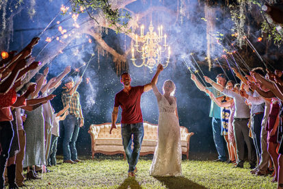 bride and groom exiting reception through a tunnel of sparklers held by friends and family