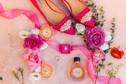wedding ring in fuschia box surrounded by pink flowers, a perfume bottle and fuschia shoes