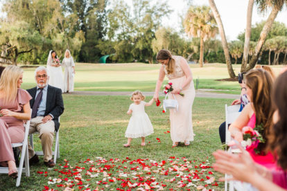 bridesmaid holding flower girl's hand as she walks down the aisle at an outdoor wedding