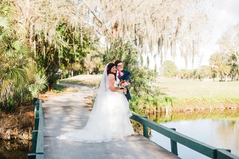 bride and groom standing on a bridge overlooking a pond