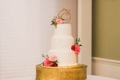wedding cake decorated with gold monogram topper and pink flowers