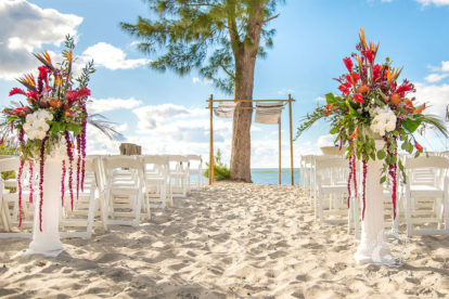 wedding ceremony on beach with large viabrant flower arrangements on columns