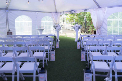 wedding ceremony setup with white chairs, lanterns and columns
