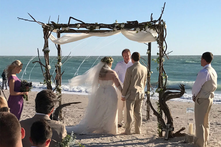 bride and groom standing in front of driftwood arbor