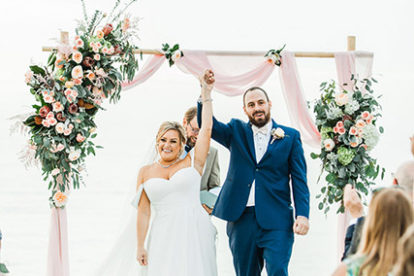 bride and groom standing in front of bamboo arbor draped in pink fabric