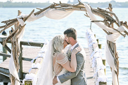 bride and groom standing on a dock under a wooden arbor