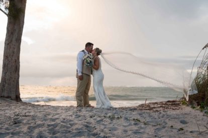 bride and groom kissing on beach with veil flying in the wind