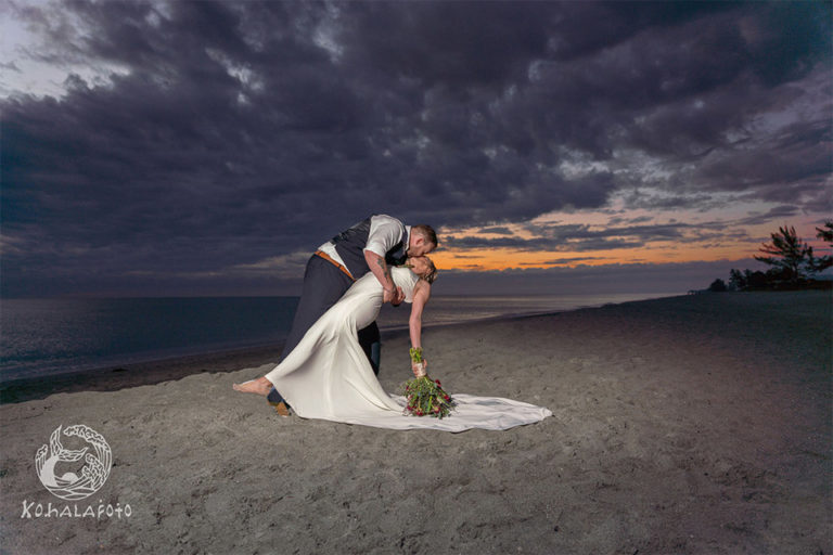 Bride and groom kissing on under a dramatic sky on the beach