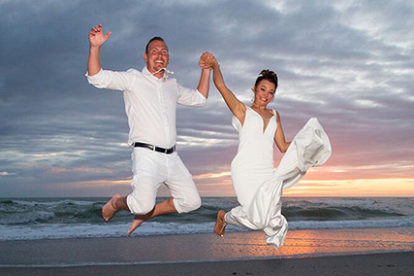 bride and groom jumping on beach at sunset