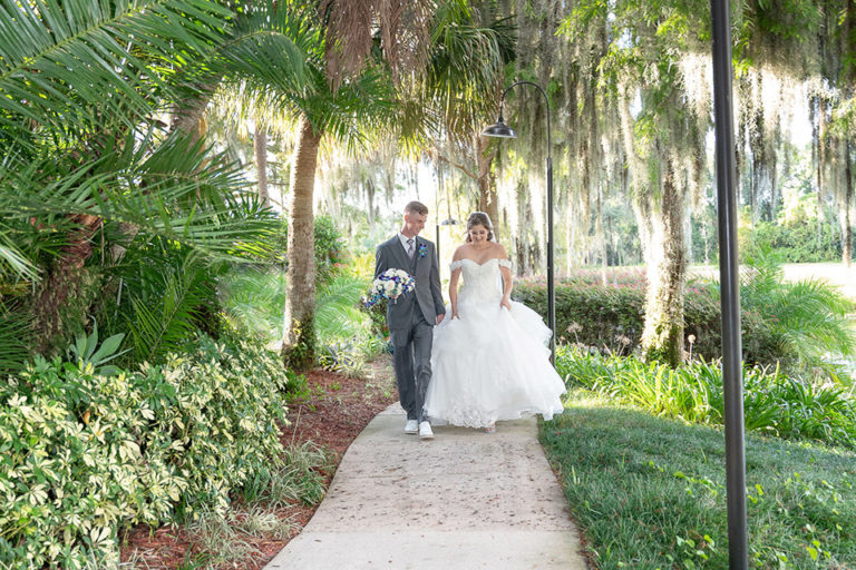 bride and groom walking together outdoors down a foliage lined path