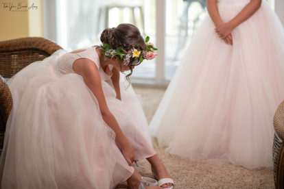 junior bridesmaid in pink dress with floral headband fastening her shoes