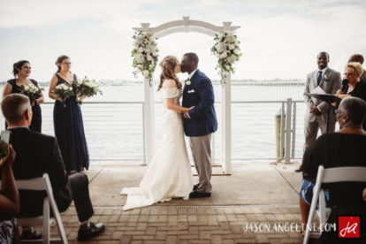 bride and groom kissing as wedding party smiles