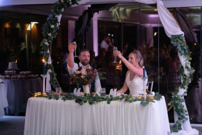 bride and groom sitting at their sweetheart table raising their glasses for a toast