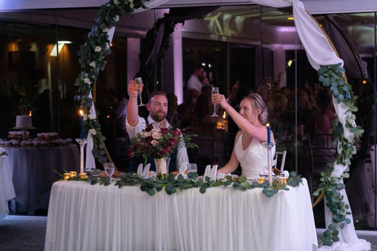 bride and groom sitting at their sweetheart table raising their glasses for a toast