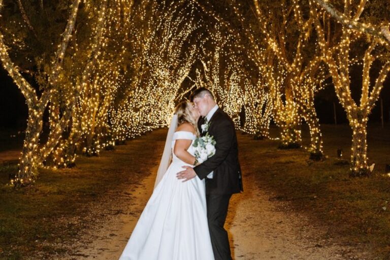 bride and groom kissing under a canopy of oak trees with white lights