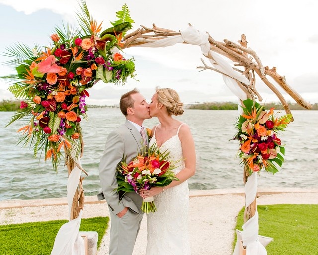bride and groom kissing under a flower-decorated arbor by the intracoastal waterway