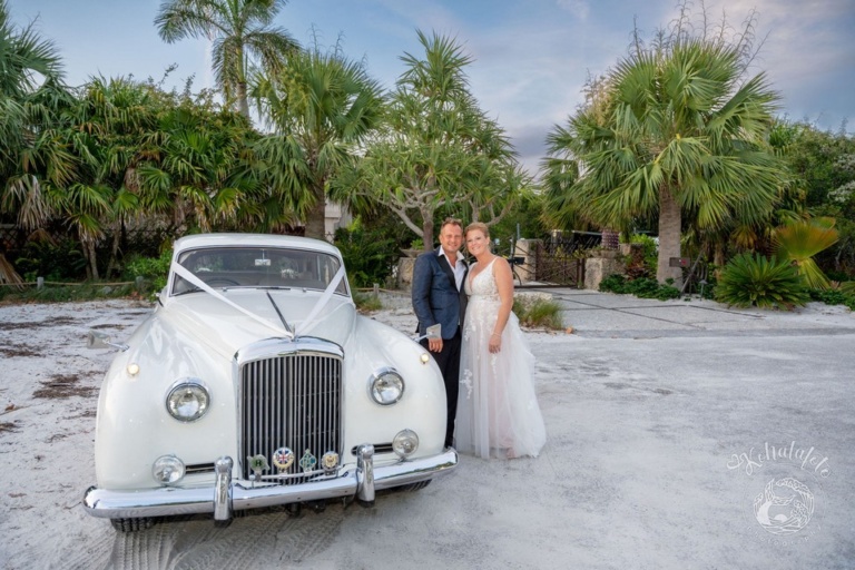 bride and groom standing beside an antique car near the beach