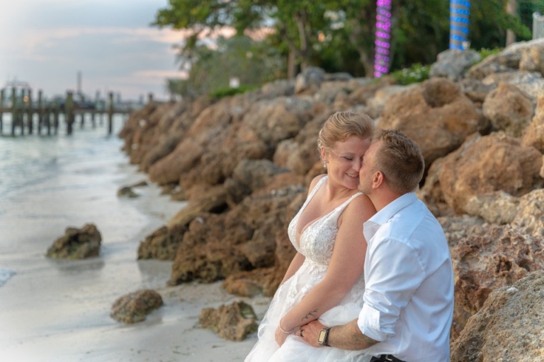 bride and groom cuddling, sitting on coquina rocks near the water