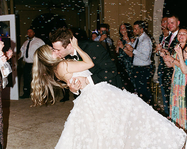 bride and groom kissing while guests blow bubbles around them